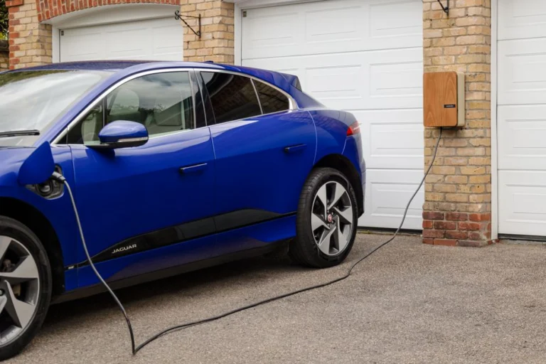 Borne de recharge murale installée à côté d'un garage, voiture électrique en charge